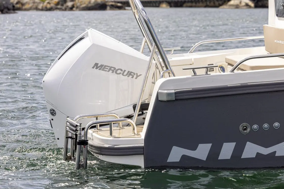 A close-up of a Mercury outboard motor mounted on the back of a Nimbus boat, floating in calm water.